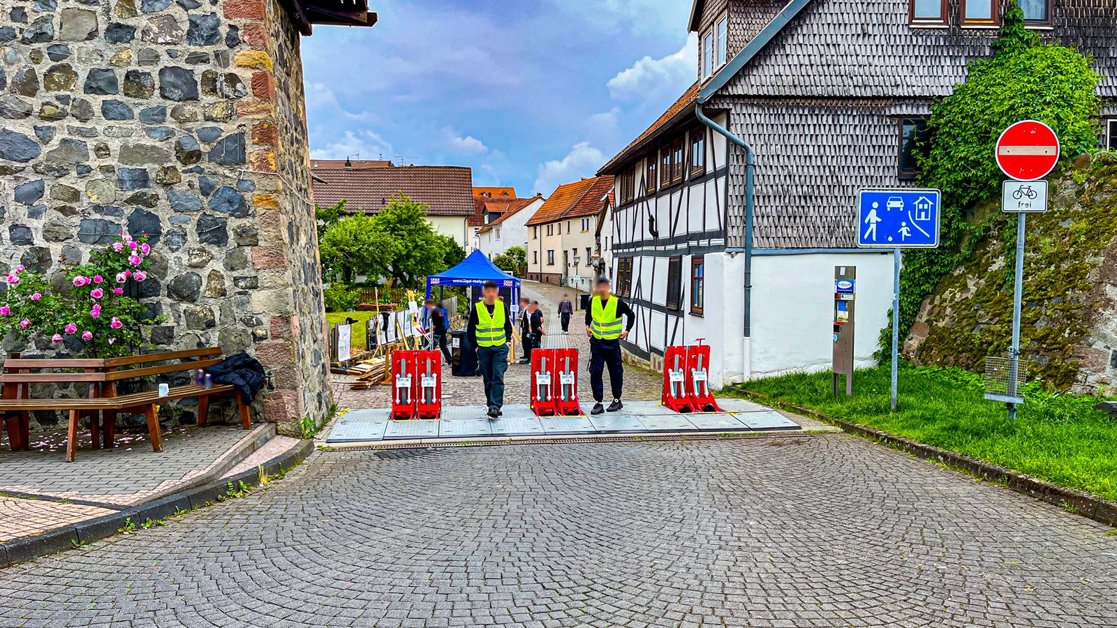 Mobile Fahrzeugsperren an der Zufahrt zu einer Altstadtgasse, davor Sicherheitskräfte